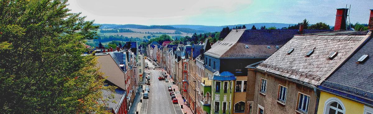 Ein Bild einer Straße aus erhöhter Perspektive zeigt merhstöckige Gebäude, eine Straße mit Fahrspuren, Gehwege, Laternen, und Fußgänger unter teilweise bewölktem Himmel. Ein Bild einer Straße aus erhöhter Perspektive zeigt merhstöckige Gebäude, eine Straße mit Fahrspuren, Gehwege, Laternen, und Fußgänger unter teilweise bewölktem Himmel.