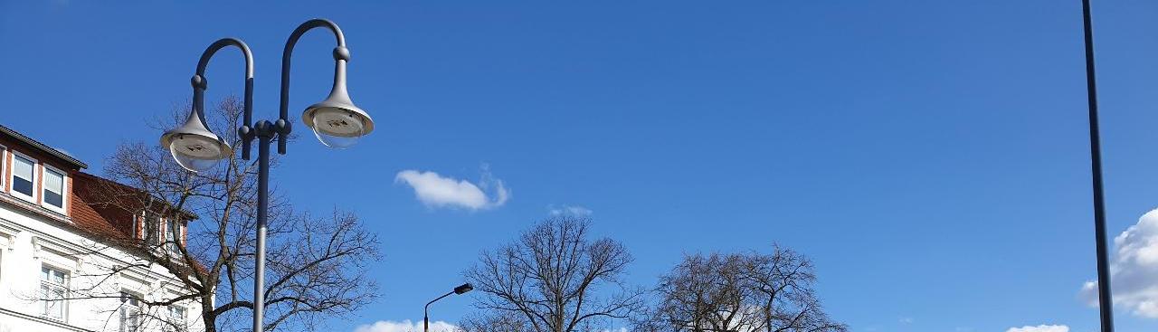 Stadtszene mit klarem Himmel, Gehweg mit Bäumen und Straßenlaternen, links ein weißes Gebäude mit rotem Dach. Stadtszene mit klarem Himmel, Gehweg mit Bäumen und Straßenlaternen, links ein weißes Gebäude mit rotem Dach.