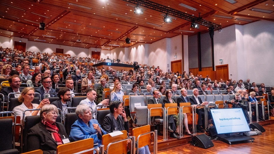 Ein Hörsaal mit ca. 400 Teilnehmenden wird von der Seite fotografiert. Ein Hörsaal mit ca. 400 Teilnehmenden wird von der Seite fotografiert.