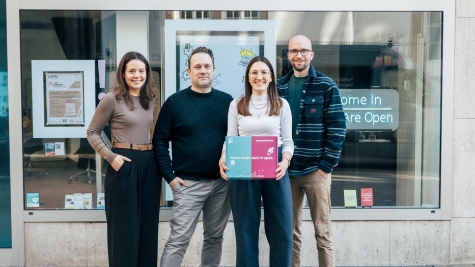 Ein Foto von vier Personen, die lächelnd in die Kamera schauen und dabei die blau-pinke Werbebox von dem Projekt „InnovateNow“ halten. Ein Foto von vier Personen, die lächelnd in die Kamera schauen und dabei die blau-pinke Werbebox von dem Projekt „InnovateNow“ halten.
