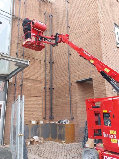 Ein rotes Kran steht neben einer Backsteinwand. Auf diesem Kran steht ein Mensch der, an der Fassade arbeitet. Ein rotes Kran steht neben einer Backsteinwand. Auf diesem Kran steht ein Mensch der, an der Fassade arbeitet.