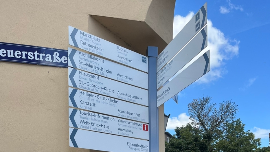 Ein Wegweiser an einer Straßenecke mit mehreren Schildern, die zu verschiedenen Sehenswürdigkeiten und Einrichtungen in der Stadt führen. Ein Wegweiser an einer Straßenecke mit mehreren Schildern, die zu verschiedenen Sehenswürdigkeiten und Einrichtungen in der Stadt führen.